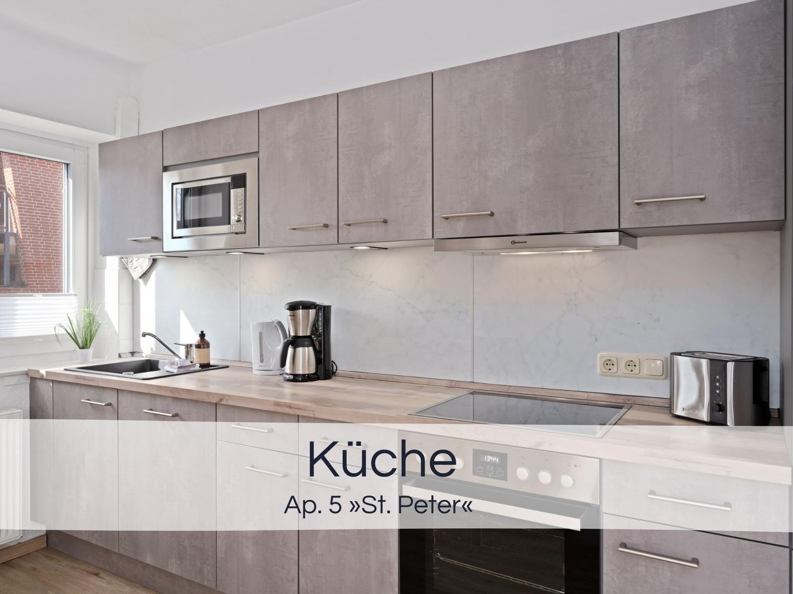 Moderne Küche mit grauen Schränken, Edelstahlgeräten und Holz Arbeitsplatte.