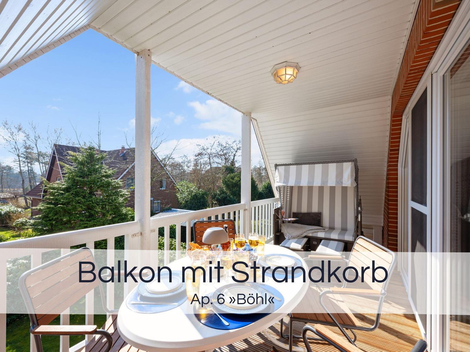 Balkon mit Tisch, Stühlen und Strandkorb. Blick auf Grünflächen und Häuser.