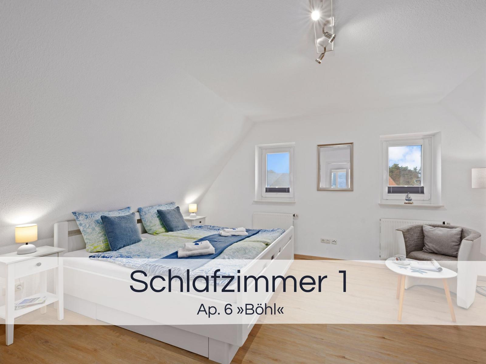 Schlafzimmer mit Doppelbett, zwei Fenstern und Sitzgelegenheit.