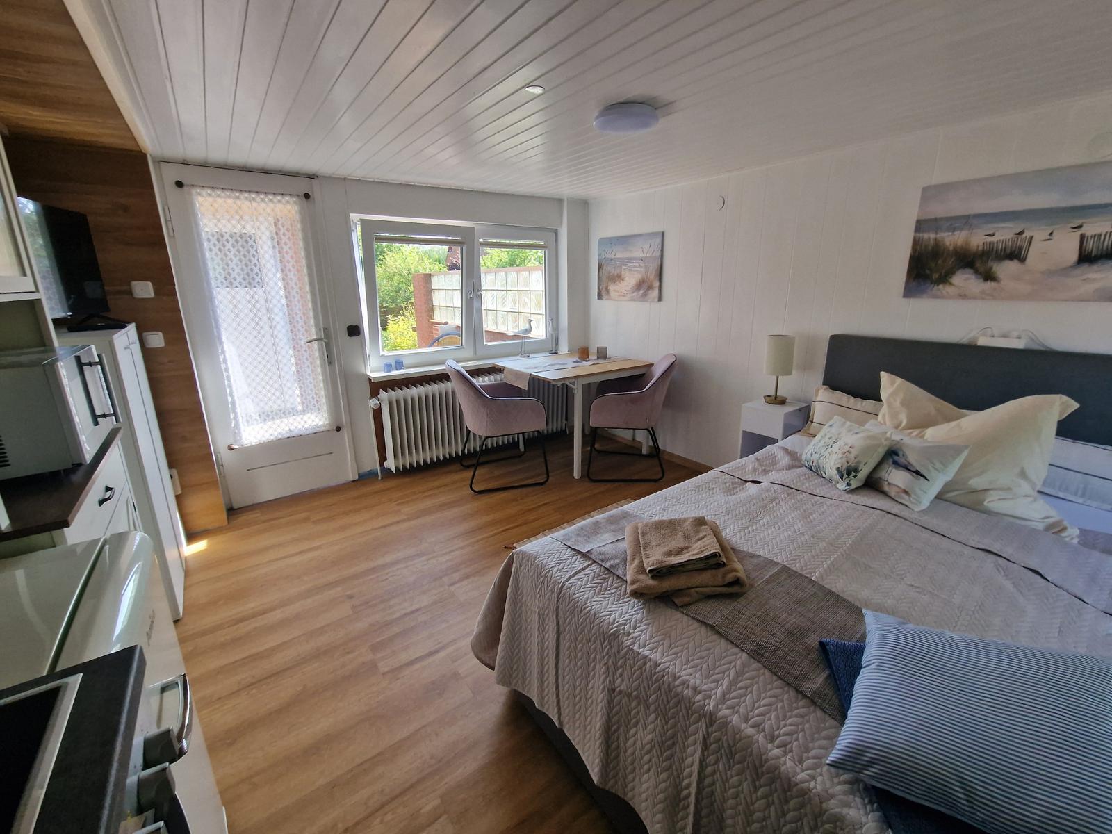 Schlafzimmer mit Bett, Schreibtisch und Fenster zur Außenterrasse.