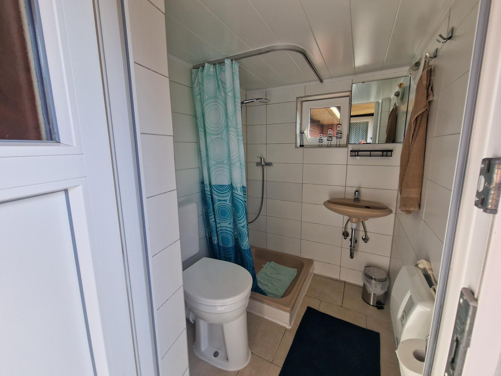 Badezimmer mit Dusche, Waschbecken und Toilette. Türkisfarbener Duschvorhang.