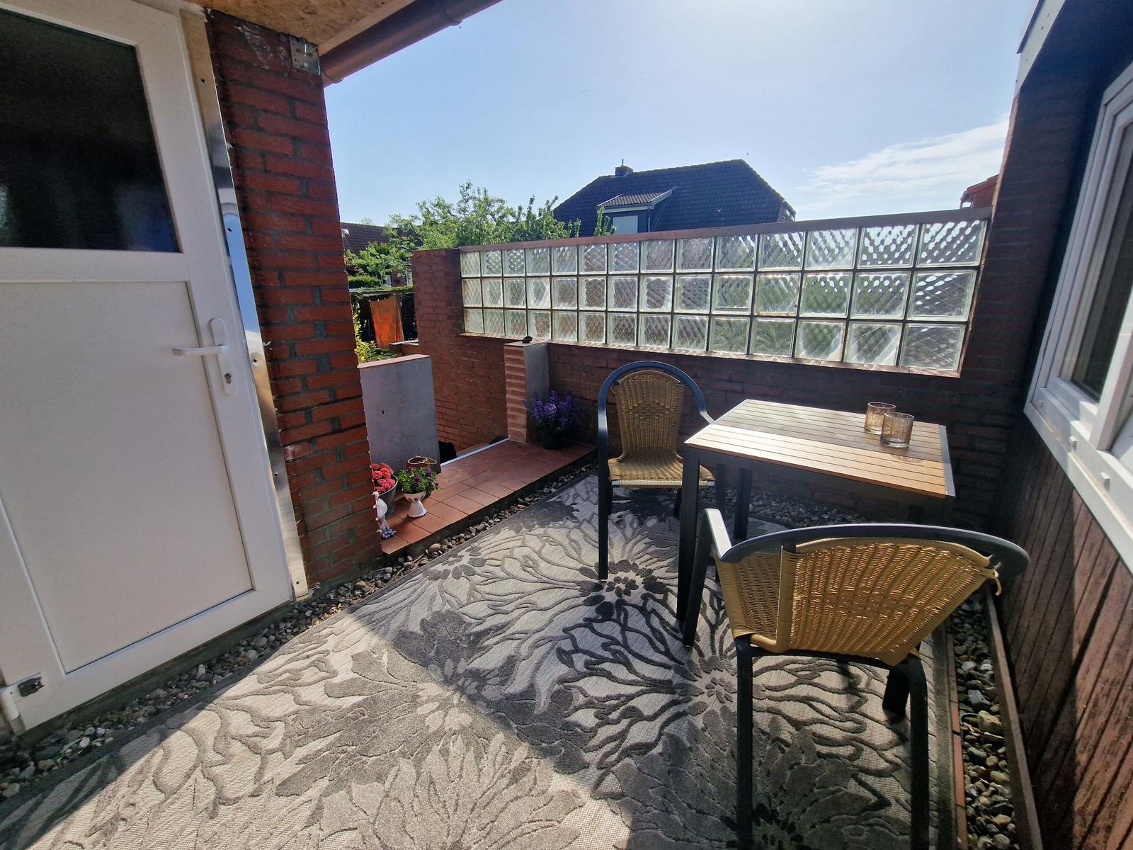 Terrasse mit Tisch, zwei Stühlen, Teppich und Glasblockwand.