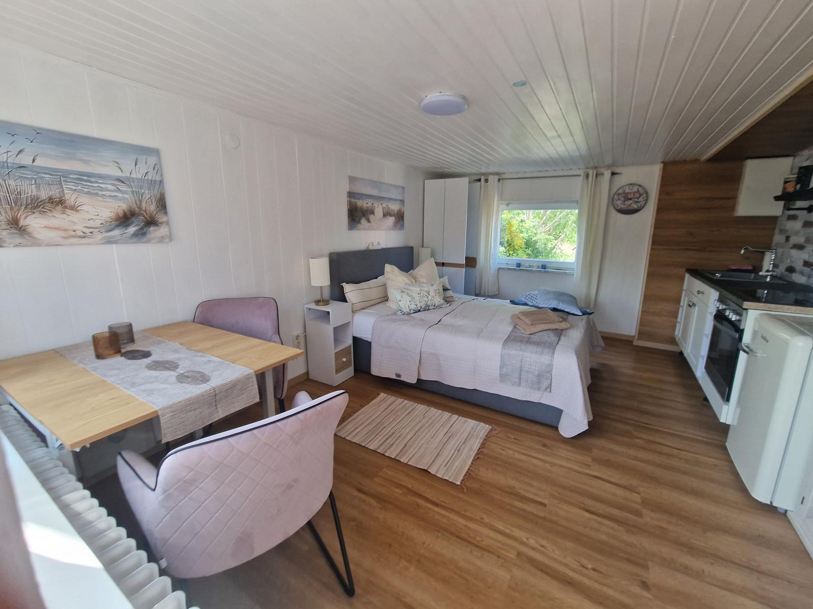 Schlafzimmer mit Bett, Esstisch, Küchenzeile und Fenster.