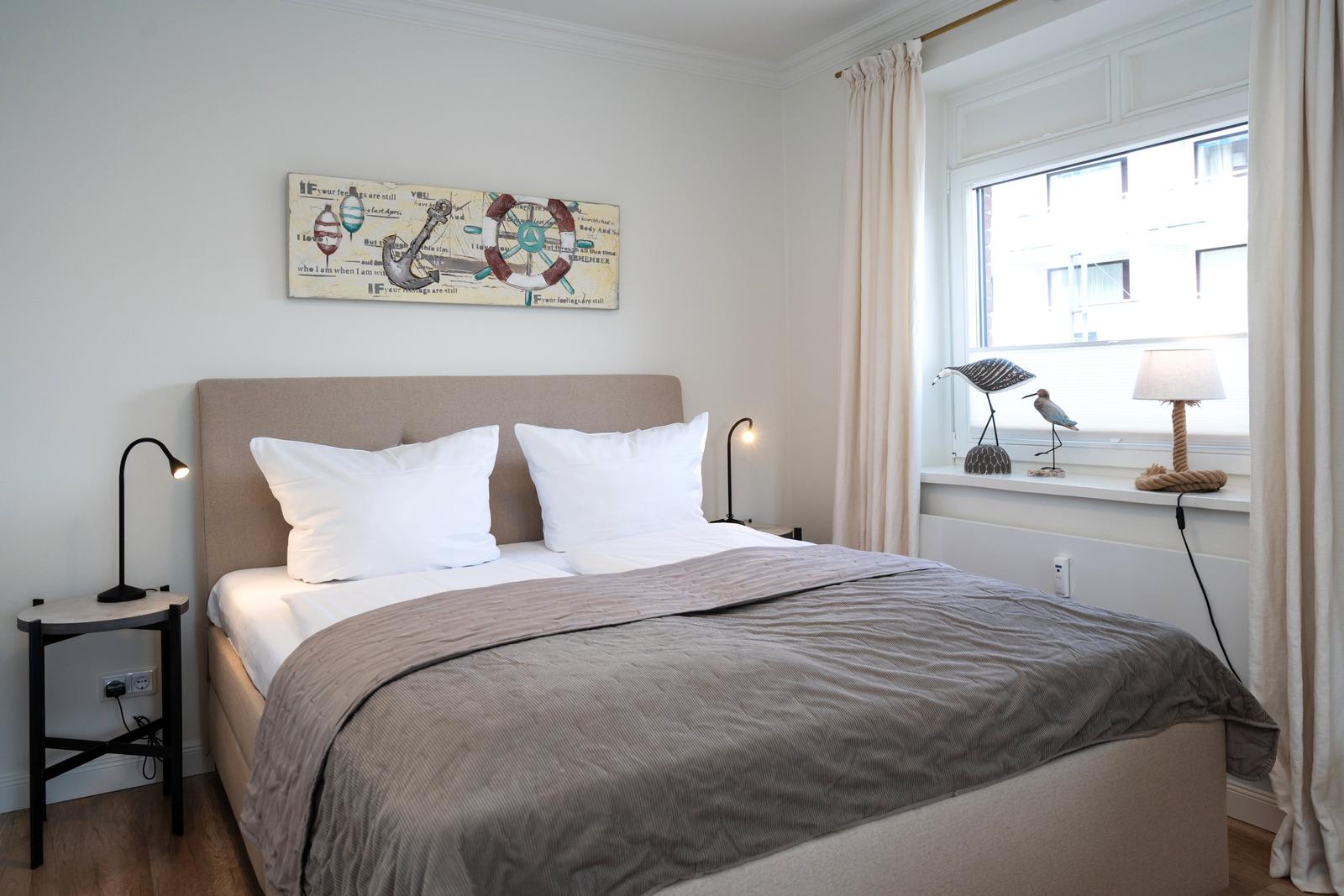 Schlafzimmer mit Bett, Nachttisch und Fenster mit Vorhängen.