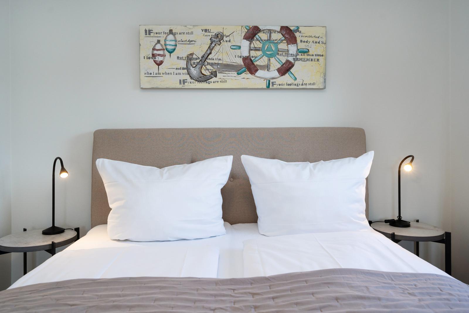 Doppelbett mit weißen Kissen und Wandbild mit Segelthema.