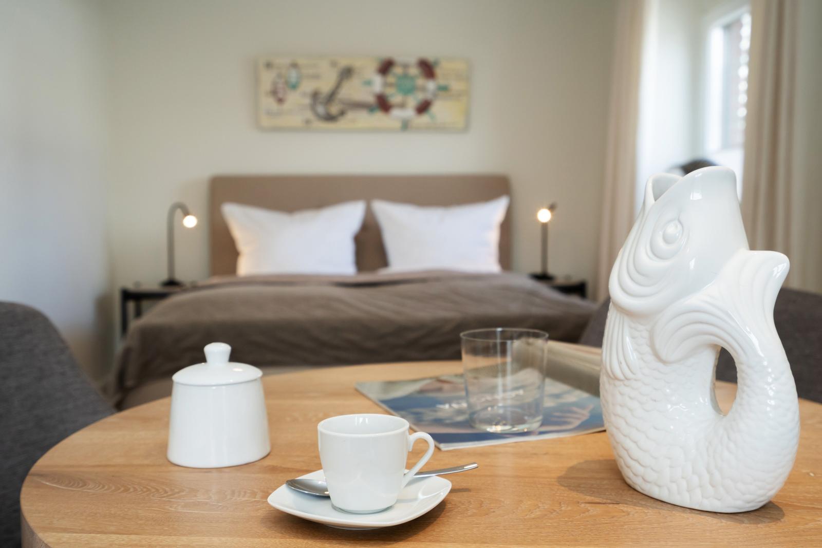 Ein Bett mit weißen Kissen und ein runder Tisch mit einer weißen Teekanne.