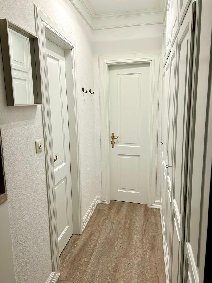 Flur mit weißen Türen, Holzboden und Haken an der Wand.