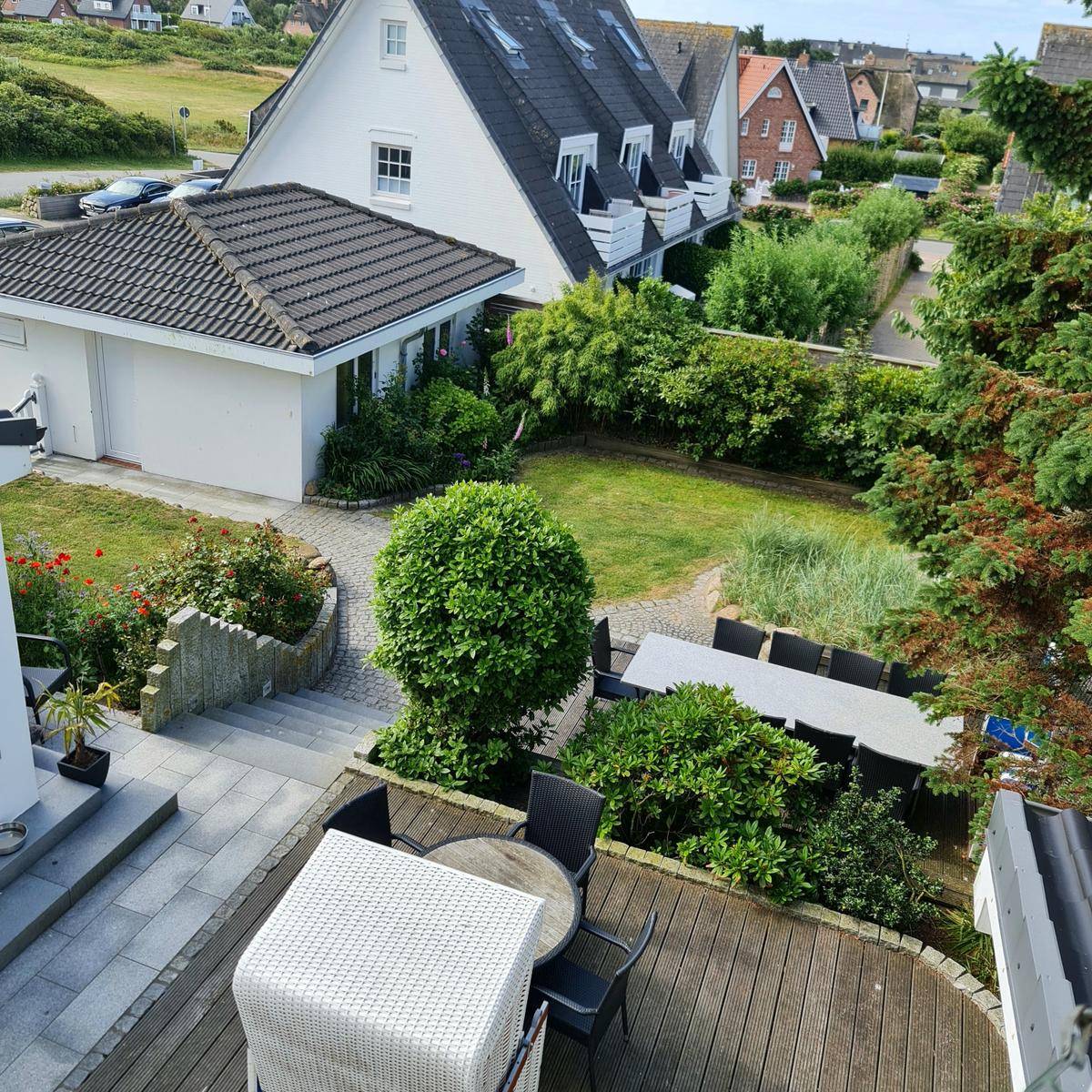 Terrasse mit Tischen und Stühlen, umgeben von Grünflächen und Häusern.