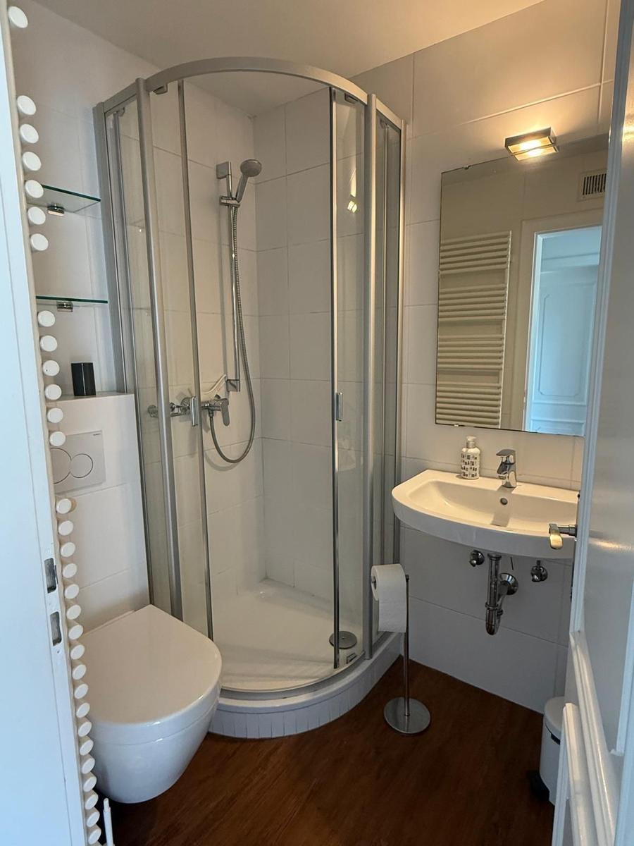 Bad mit Dusche, Waschbecken und Toilette. Holzfußboden und Spiegel.