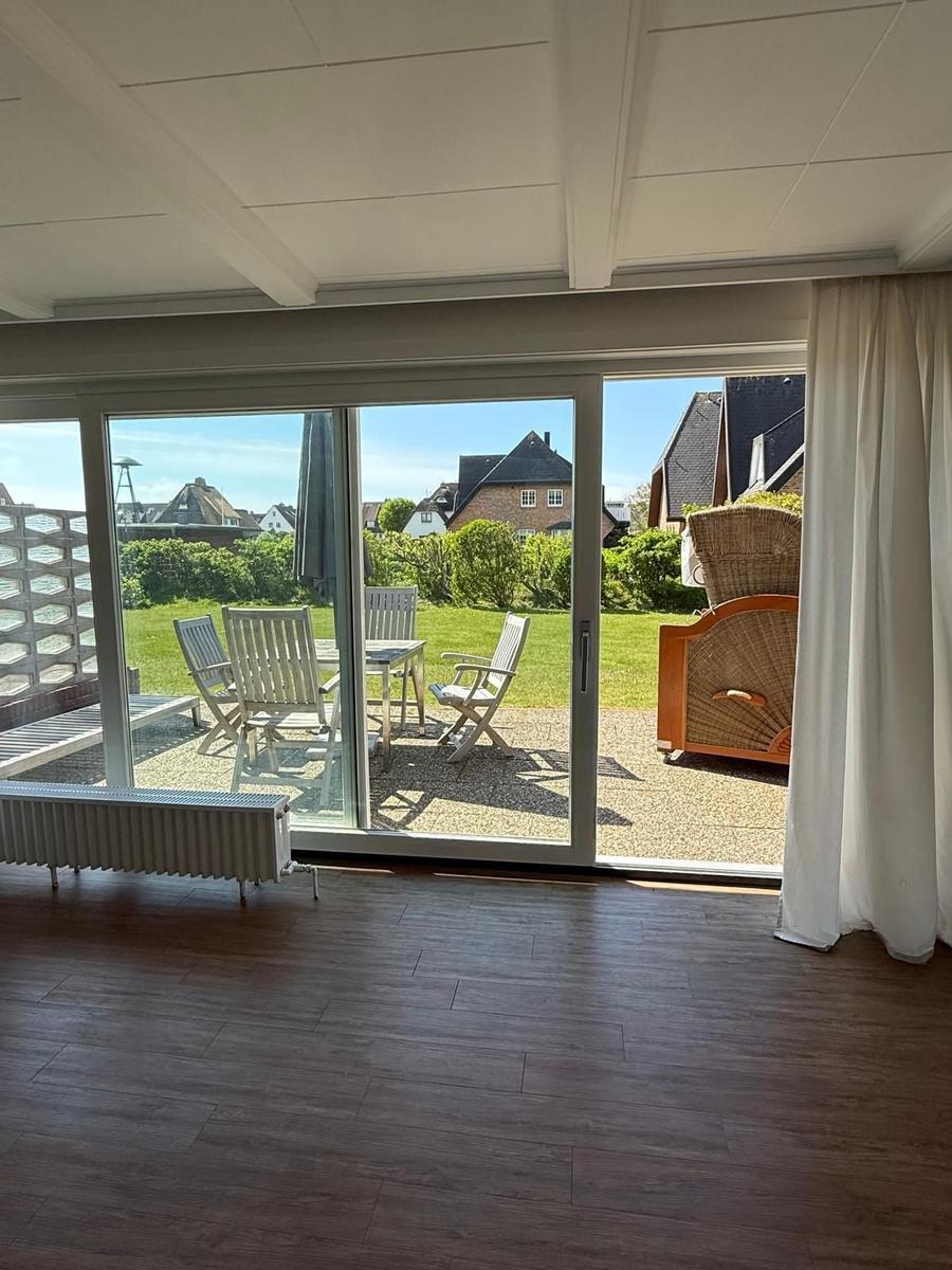 Räumlichkeiten mit Holzboden und Glasfront zum Garten mit Sitzmöbeln.