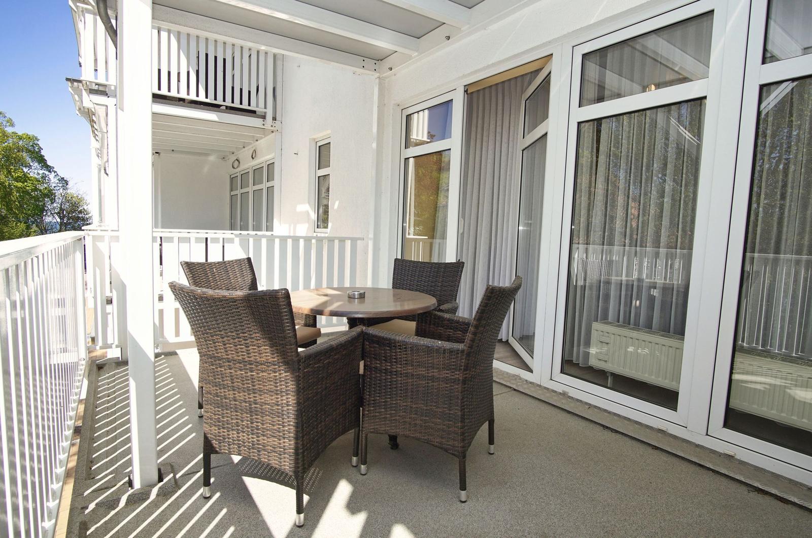 Terrasse mit Tisch und vier Stühlen, großflächige Fenster, weißer Geländer