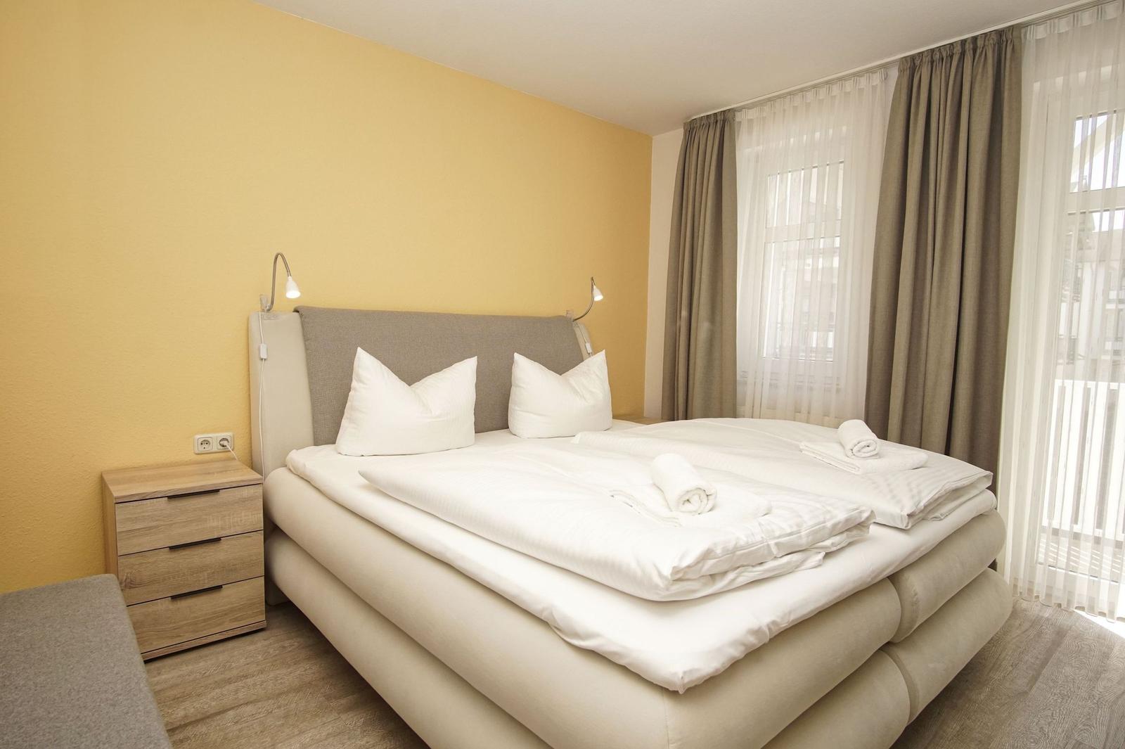 Schlafzimmer mit Doppelbett, Nachttisch und Fenster mit Vorhängen.