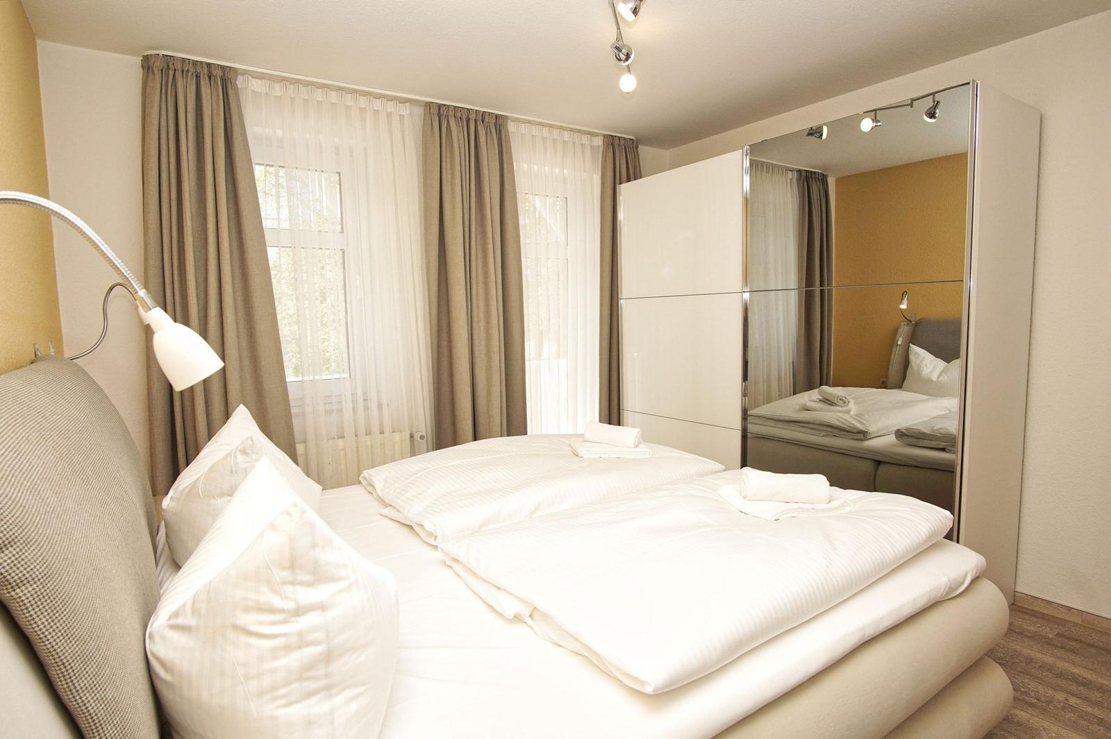 Schlafzimmer mit Doppelbett, Spiegelschrank und Fenster mit Vorhängen.