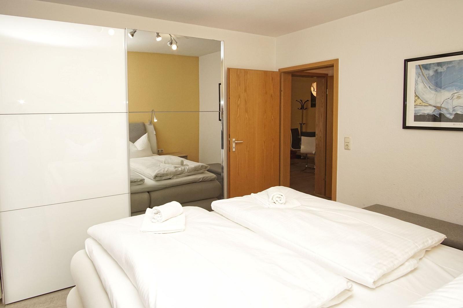 Schlafzimmer mit Bett, Spiegelschrank und angrenzender Tür.
