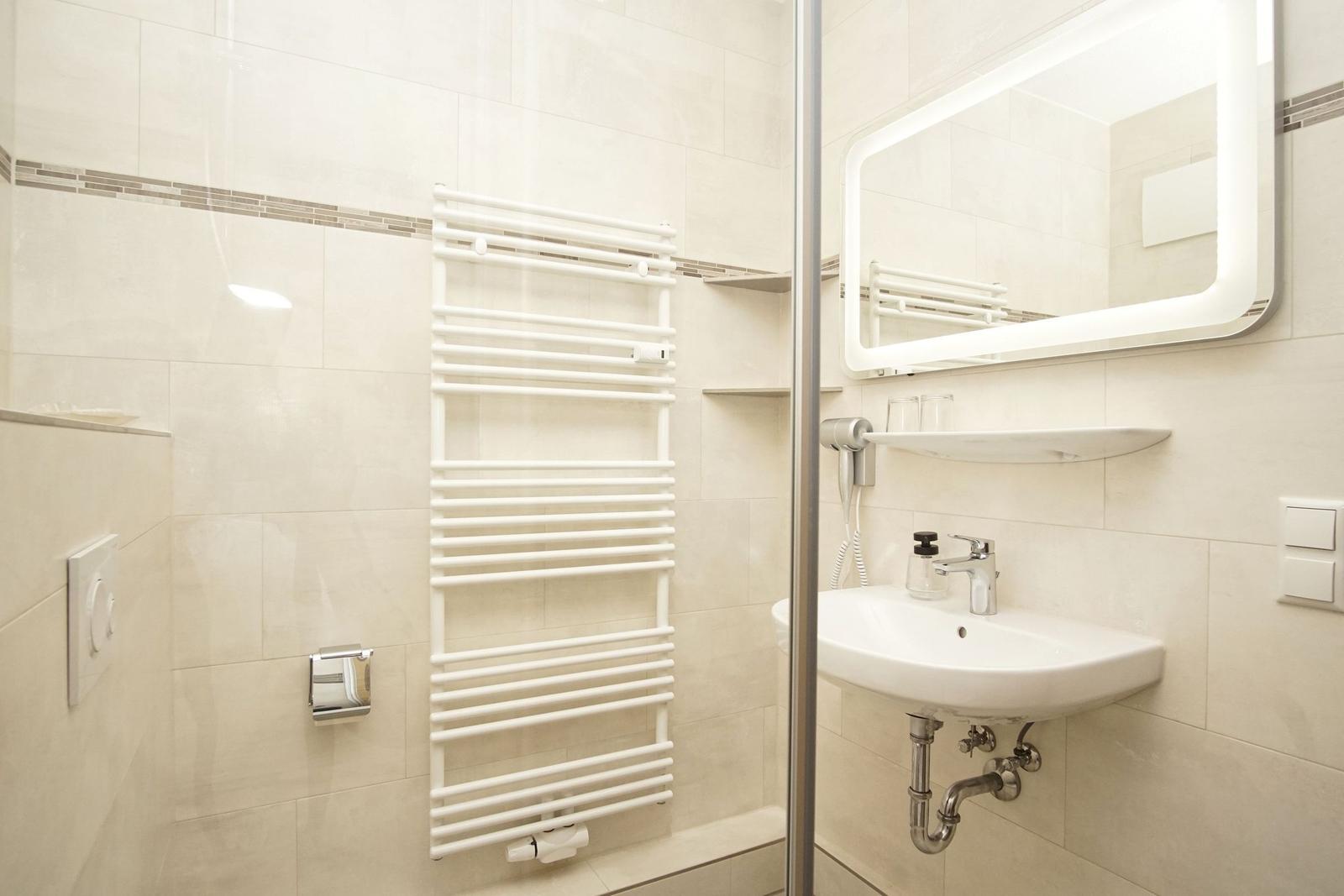 Badezimmer mit Dusche, Handtuchhalter und Waschbecken mit Spiegel.