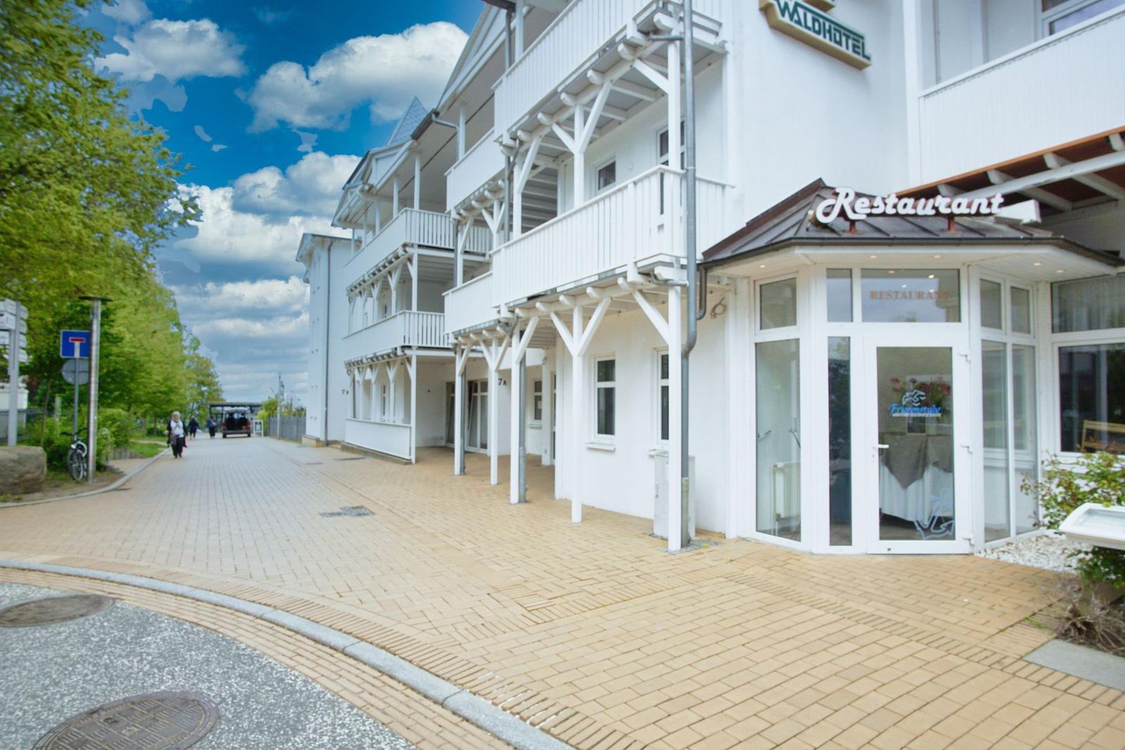 Weißes Hotel mit Restaurant und Balkonen an sonnigem Tag.