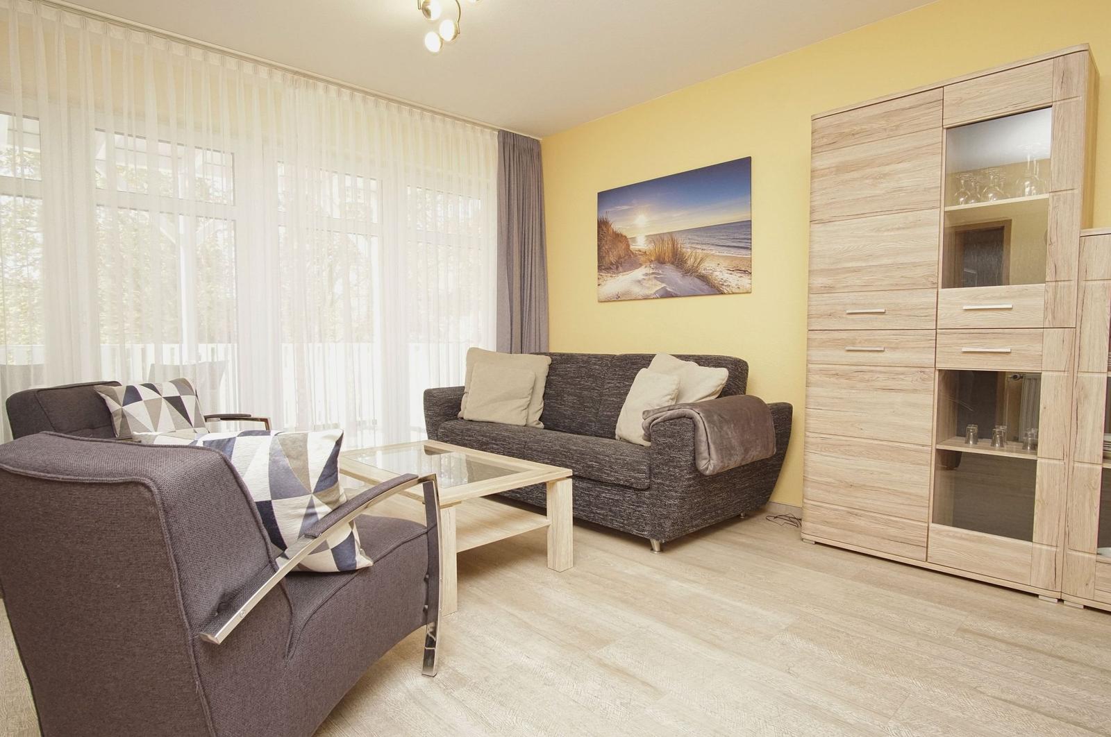 Wohnzimmer mit Sofa, Sessel, Couchtisch und Kleiderschrank. Wandbild zeigt Strand.