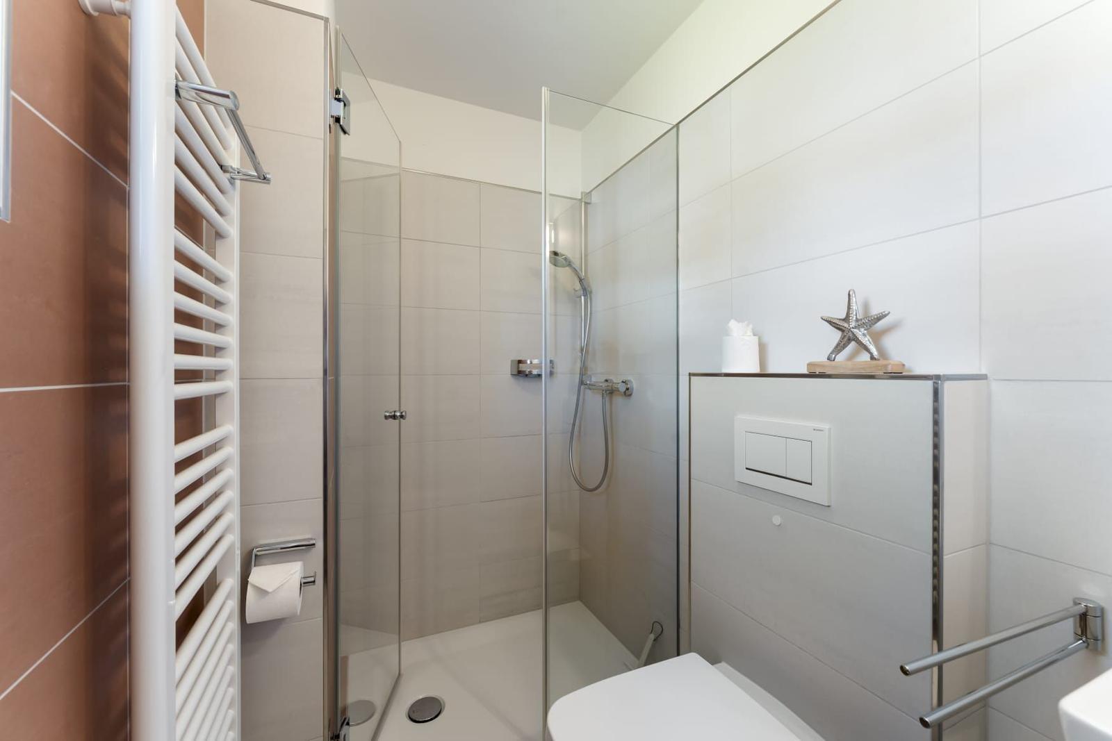 Dusche mit Glaswand, Toilette und Heizkörper an der Wand.
