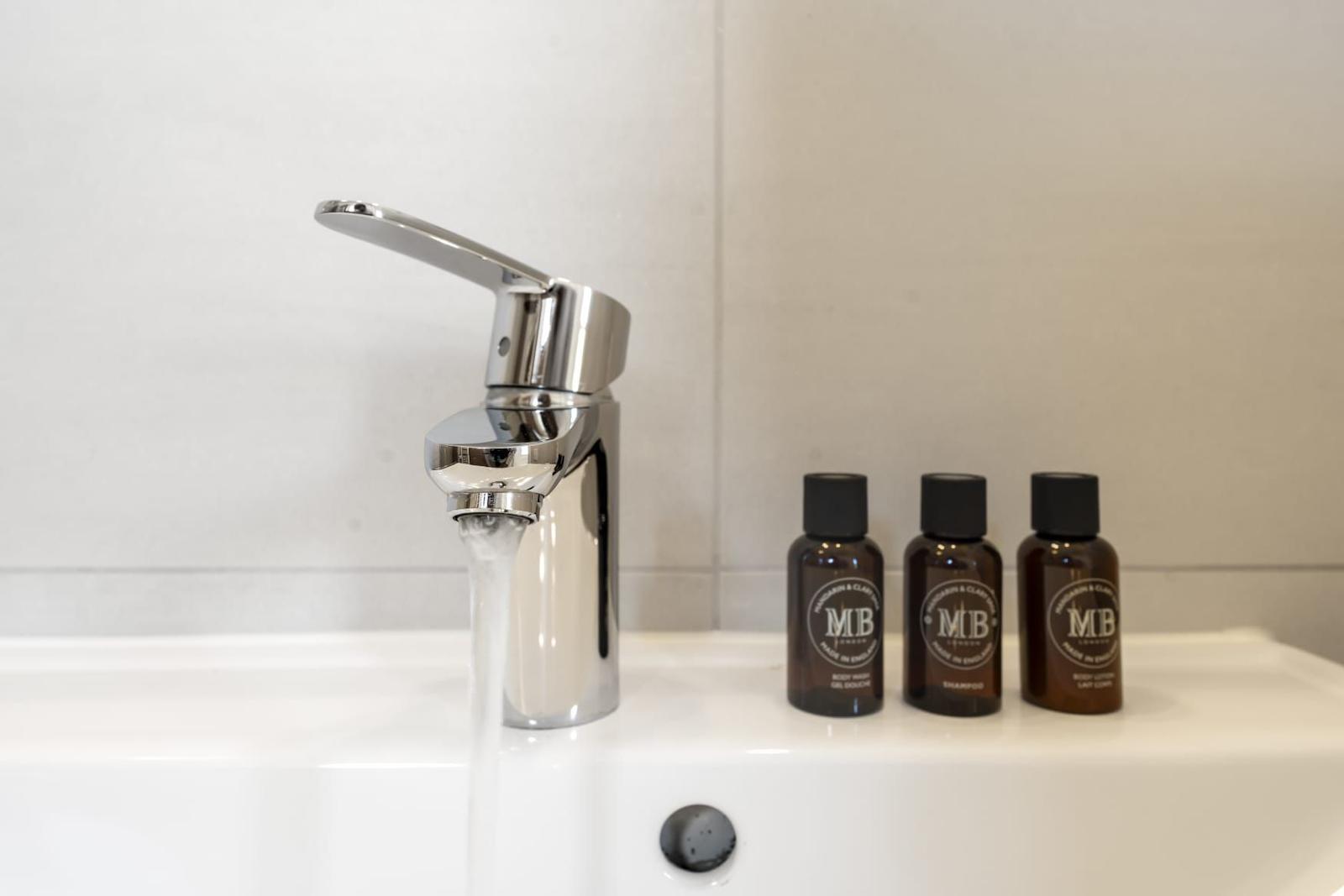 Waschbecken mit Wasserhahn und drei Flaschen mit Pflegeprodukten.