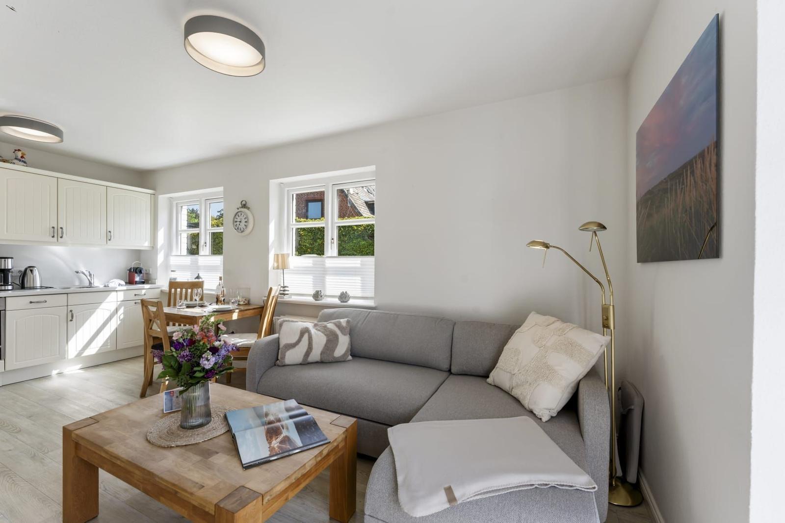 Wohnbereich mit Sofa, Esstisch und Küchenzeile. Fenster mit Blick auf Außenbereich.