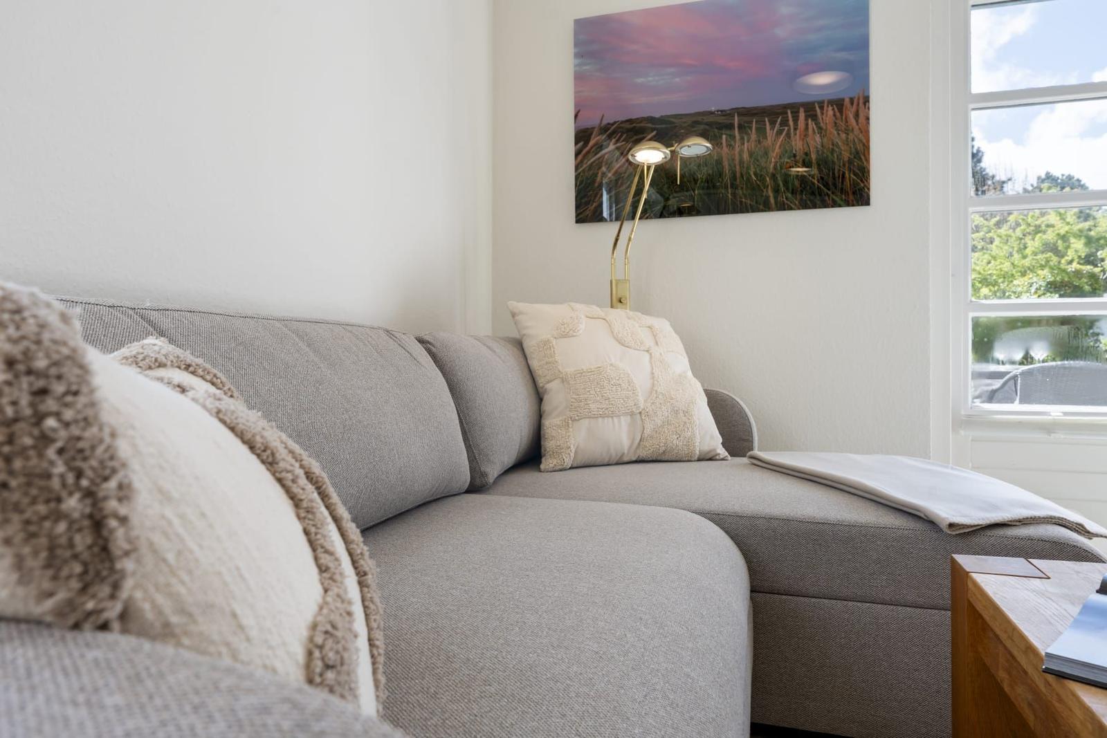 Graße Couch mit Kissen und Decke. Wandbild und Fenster mit Blick.