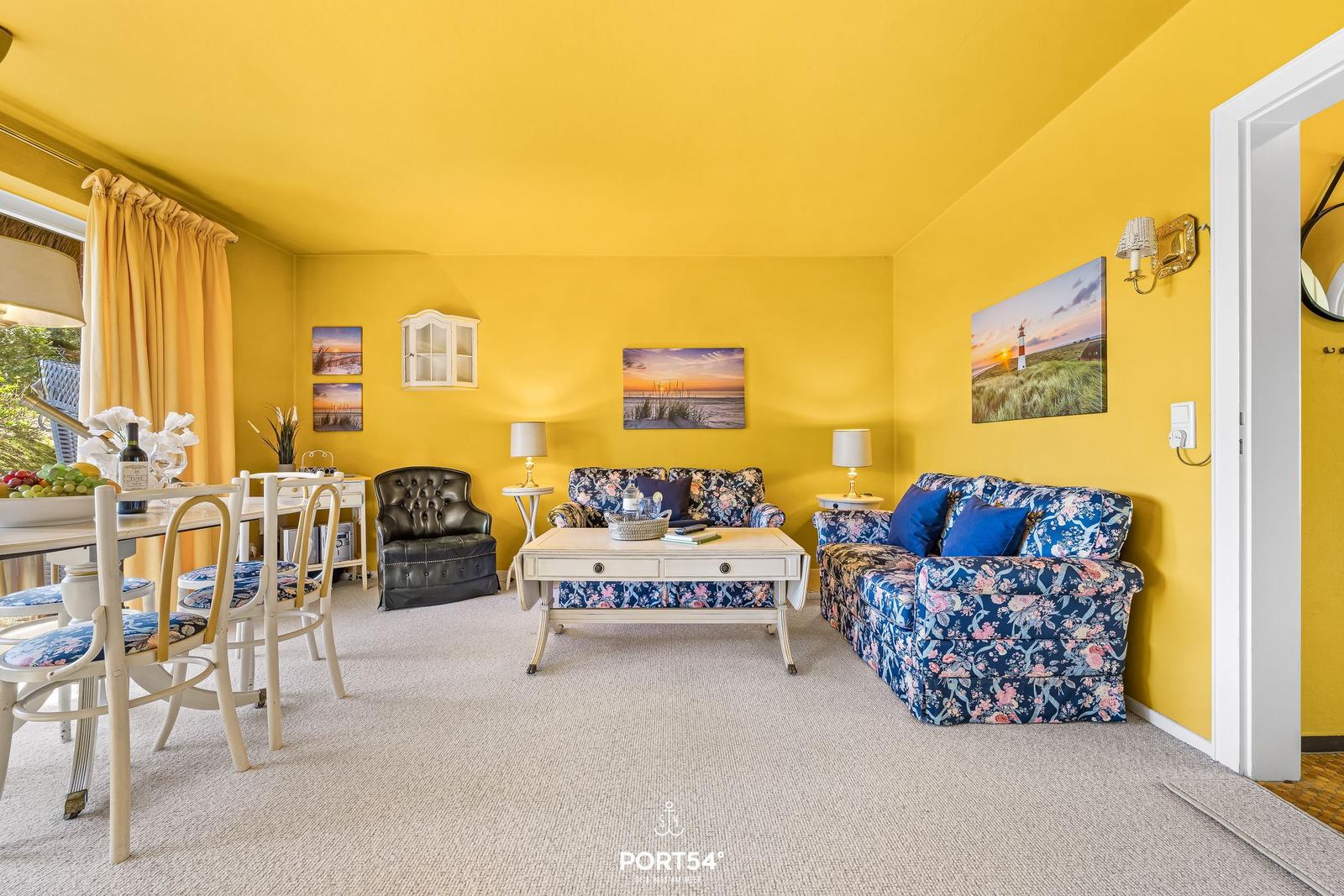Wohnzimmer mit gelben Wänden, blauem Sofa und Esstisch mit Stühlen.
