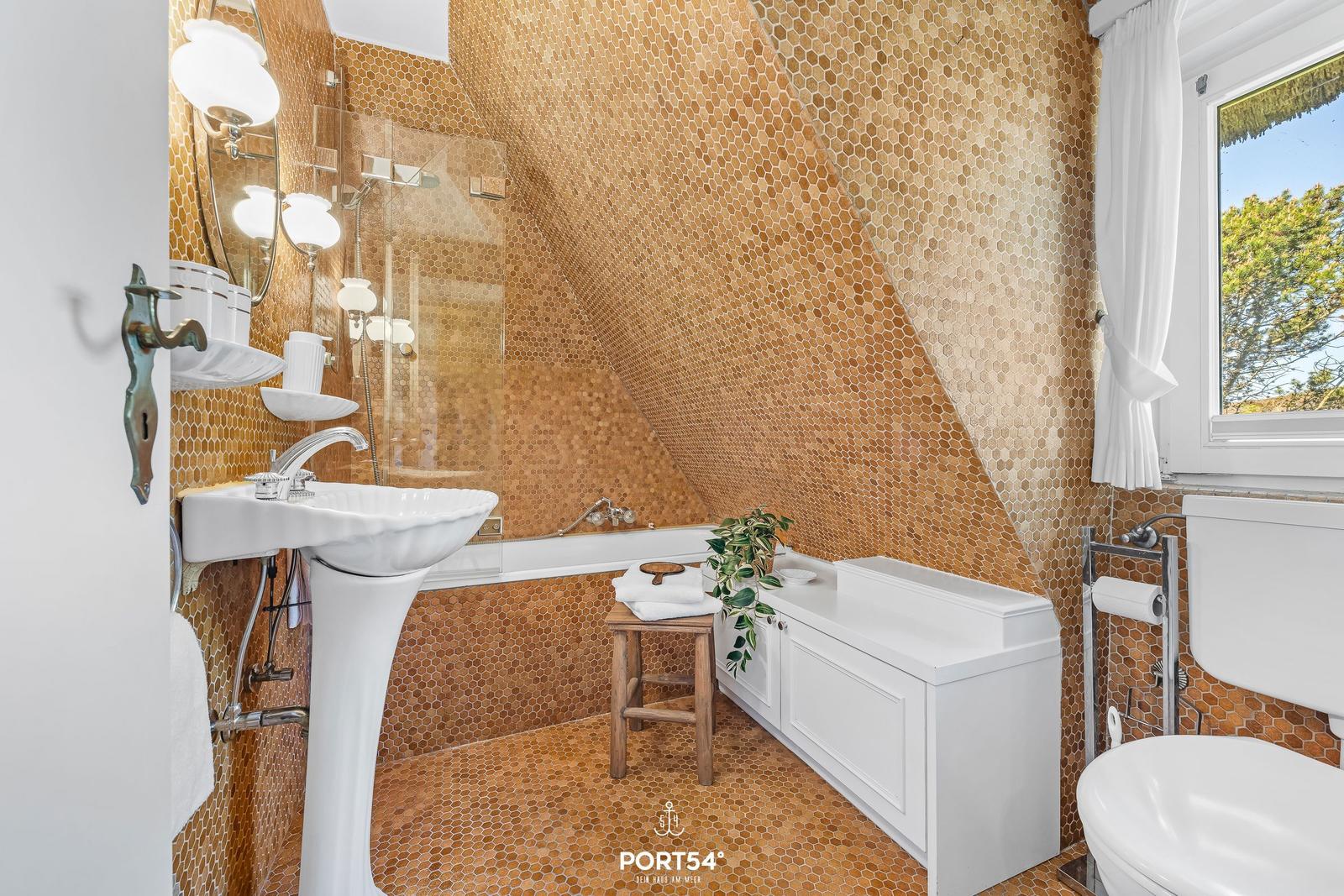 Badezimmer mit sechseckigen Fliesen, weißer Waschbecken und Badewanne unter Dachschrägen.