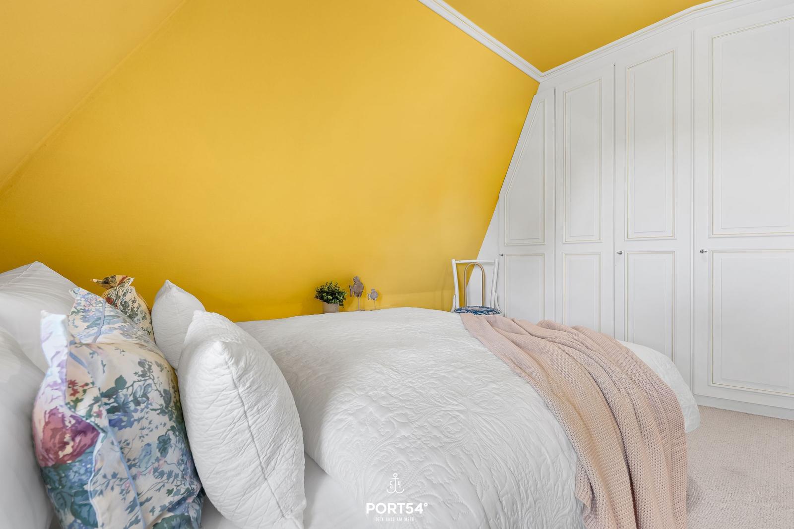 Schlafzimmer mit gelber Wand, weißem Bett und Kleiderschrank