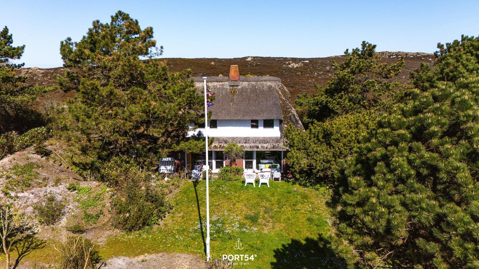 Haus mit Strohdach, Garten und weißen Stühlen unter Bäumen