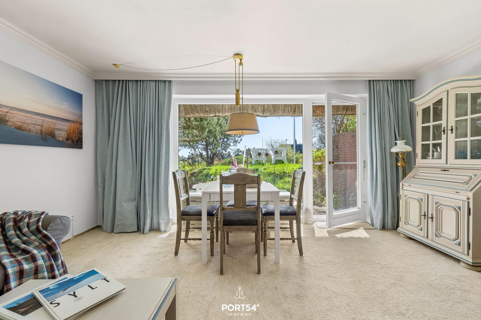 Esszimmer mit Tisch, Stühlen und Blick auf Garten. Vorhang und Schrank sind sichtbar.
