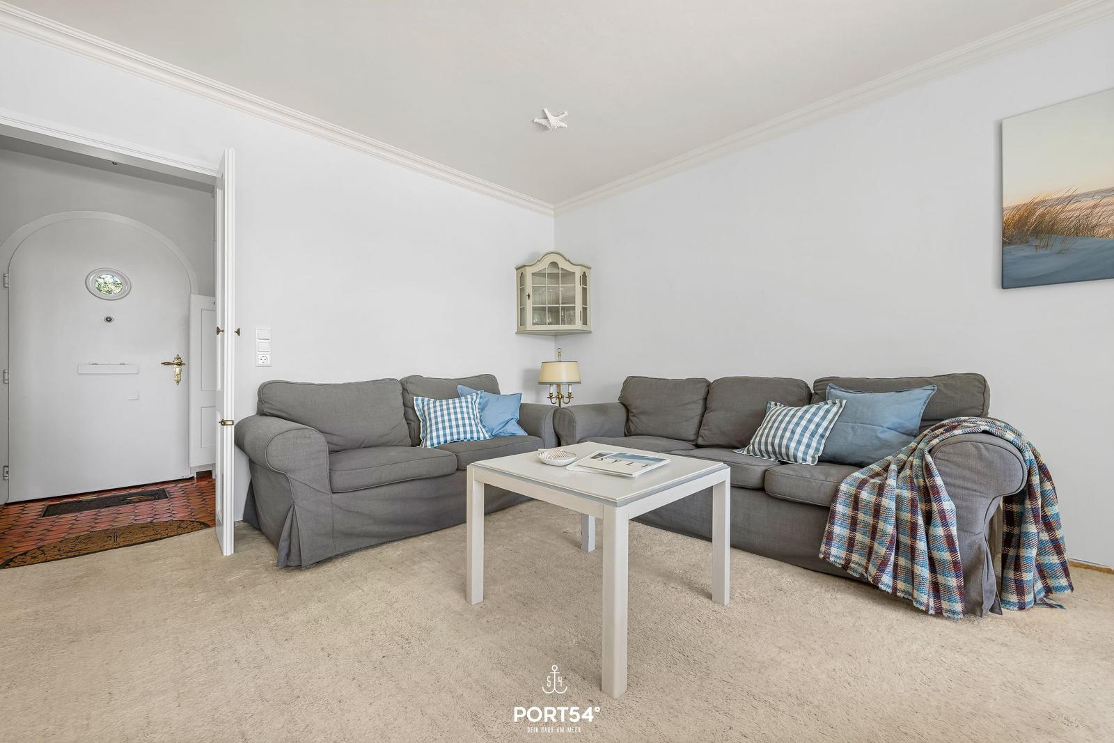 Wohnzimmer mit grauem Sofa, weißen Möbeln und Wandbild.