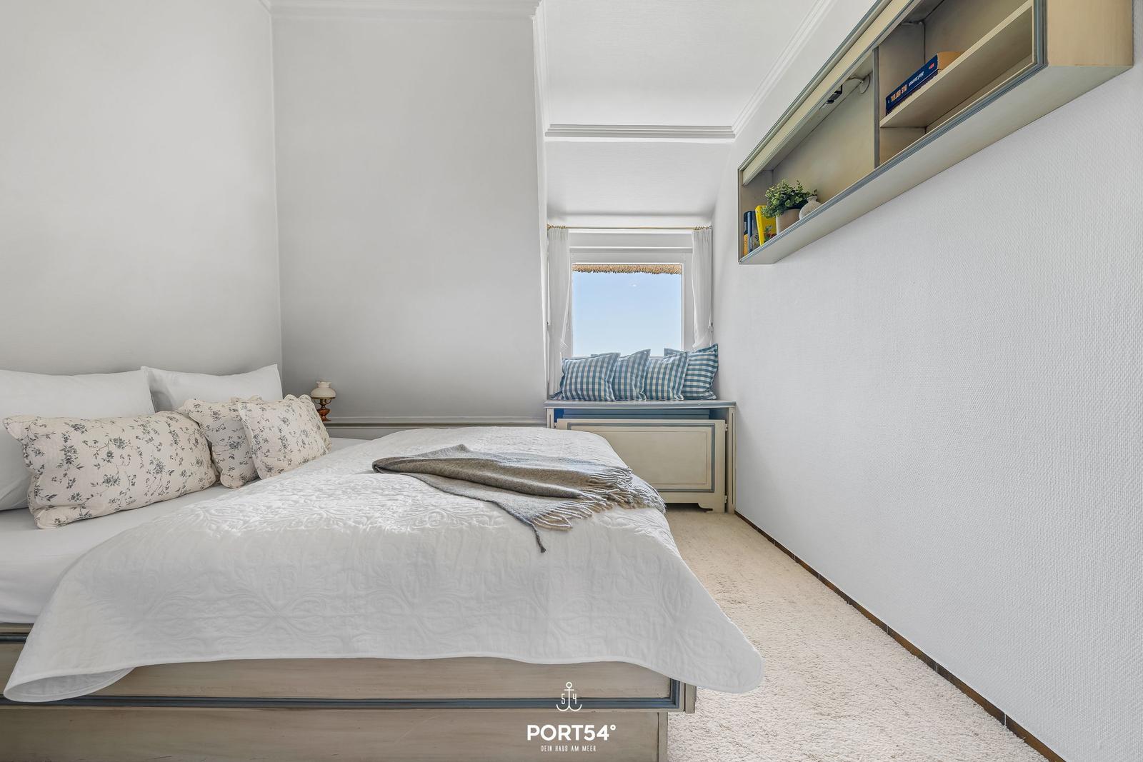 Schlafzimmer mit Bett, Fensterbank und Wandregal.