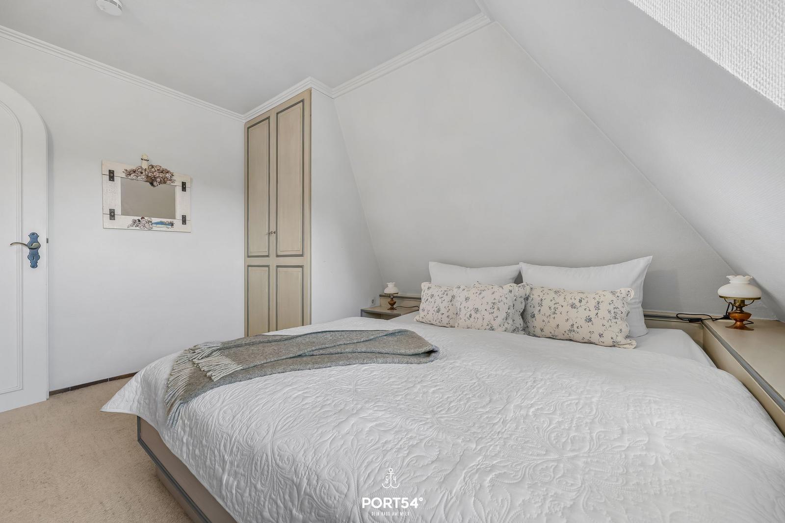 Schlafzimmer mit Dachschrägen, Bett, Kleiderschrank und Spiegel an der Wand.