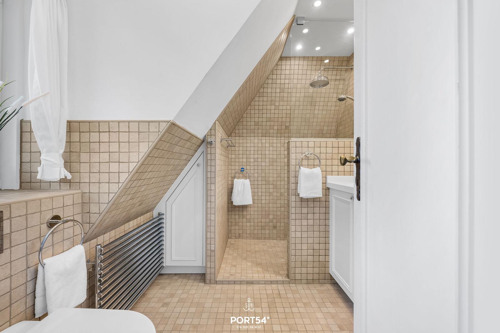 Dusche mit Duschbrause, Handtuchhalter und beigefarbenen Fliesen.