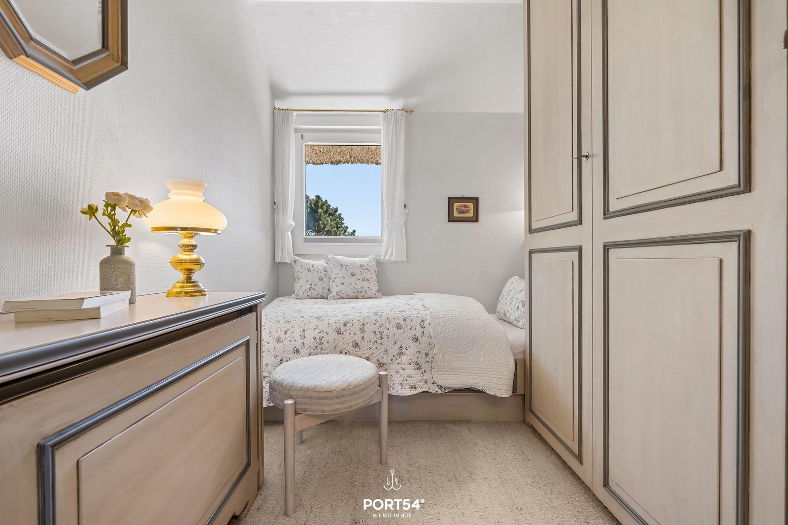 Schlafzimmer mit Bett, Schrank und Fenster mit Blick auf Bäume.