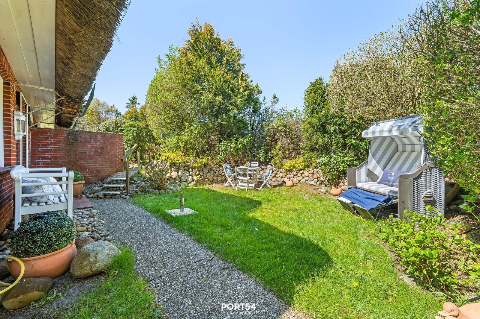 Hinterhof mit Grasfläche, Steingarten, Tisch mit Stühlen und Strandkorb.