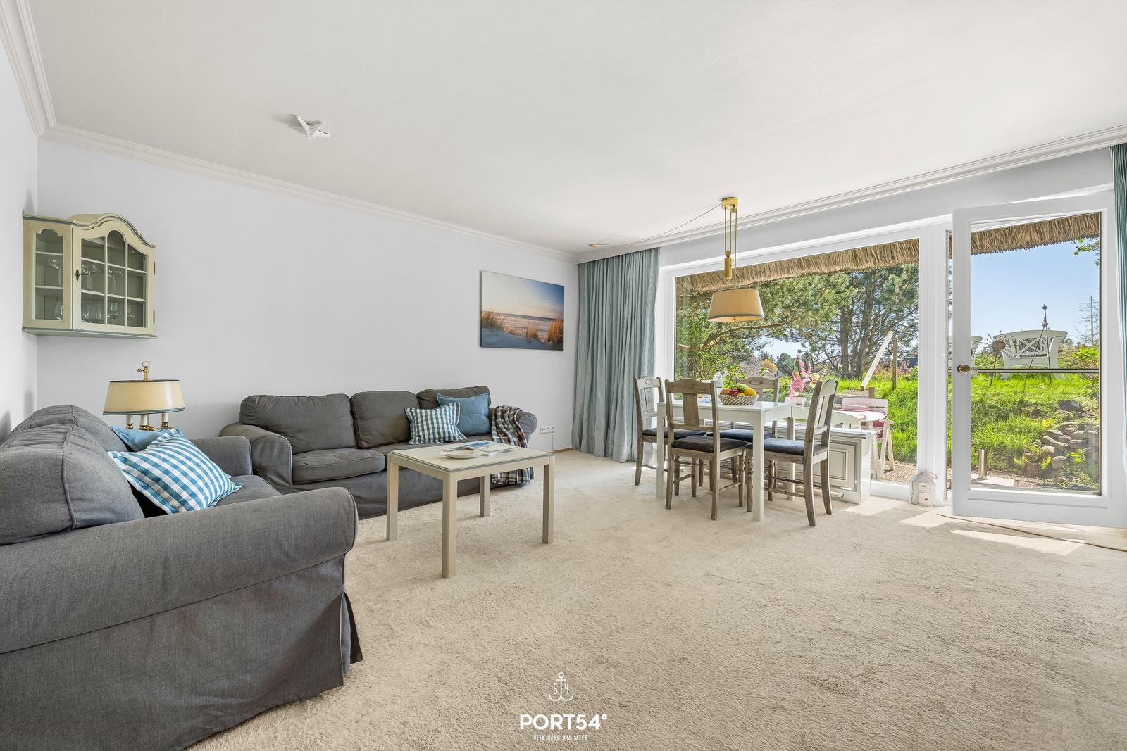 Wohn- und Essbereich mit Blick auf Garten. Sofa, Tisch und Stühle sind vorhanden.