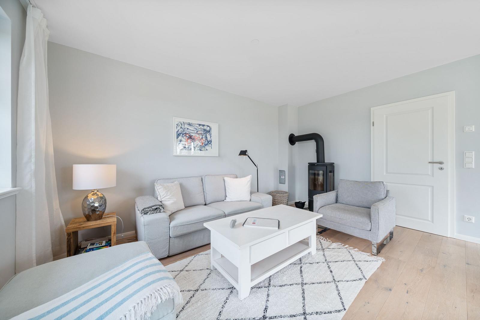 Wohnzimmer mit Sofa, Sessel, Kaminofen und Holzboden.