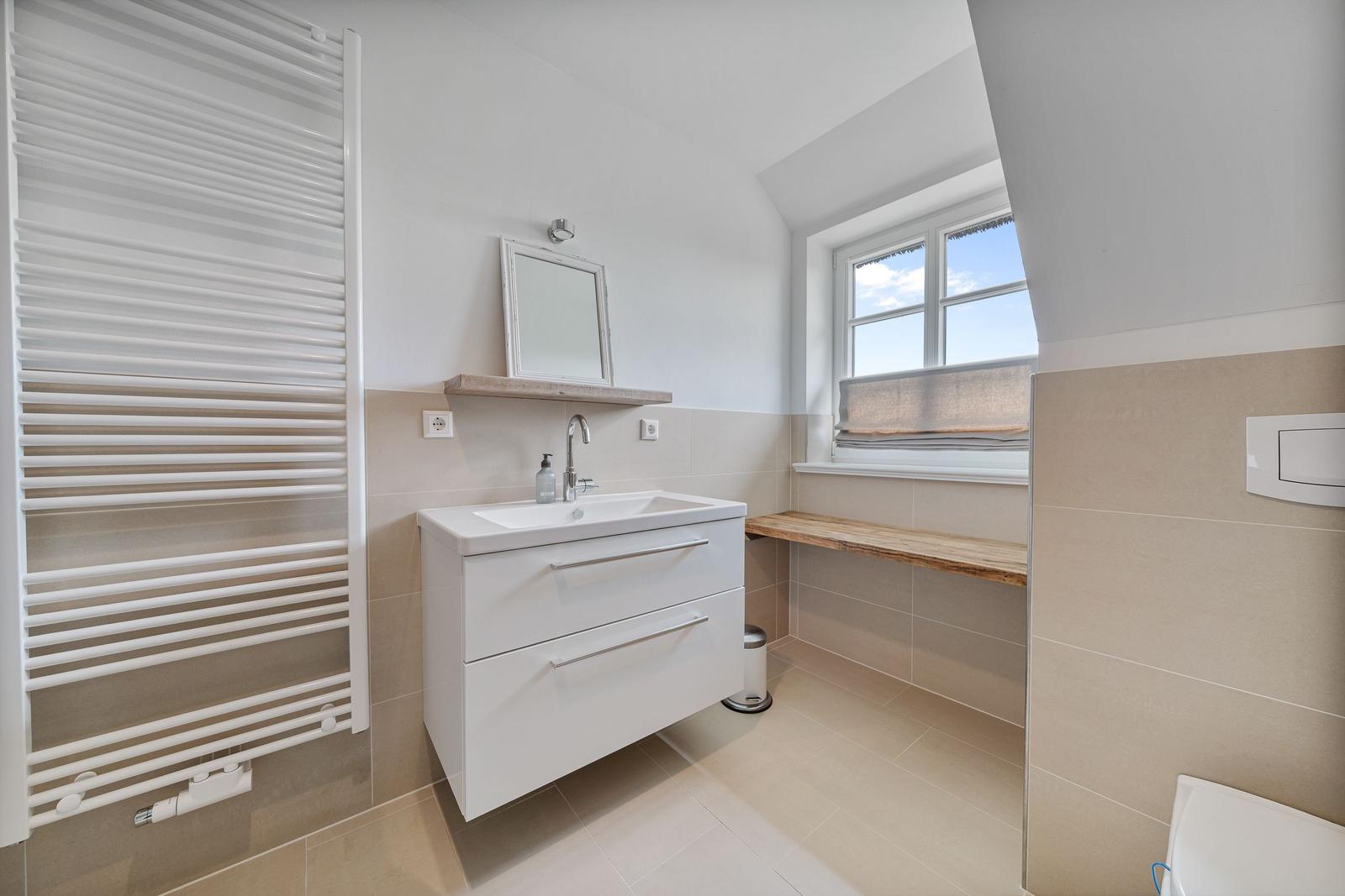 Badezimmer mit Waschbecken, Spiegel, Fenster und Heizkörper.