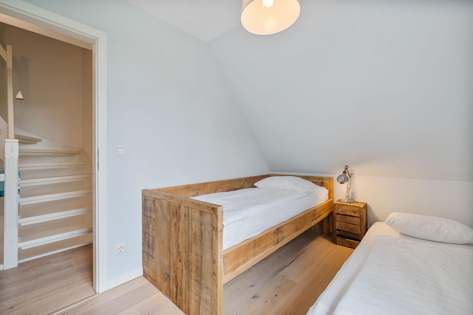 Zimmer mit zwei Betten, Holzboden und Treppe im Hintergrund.