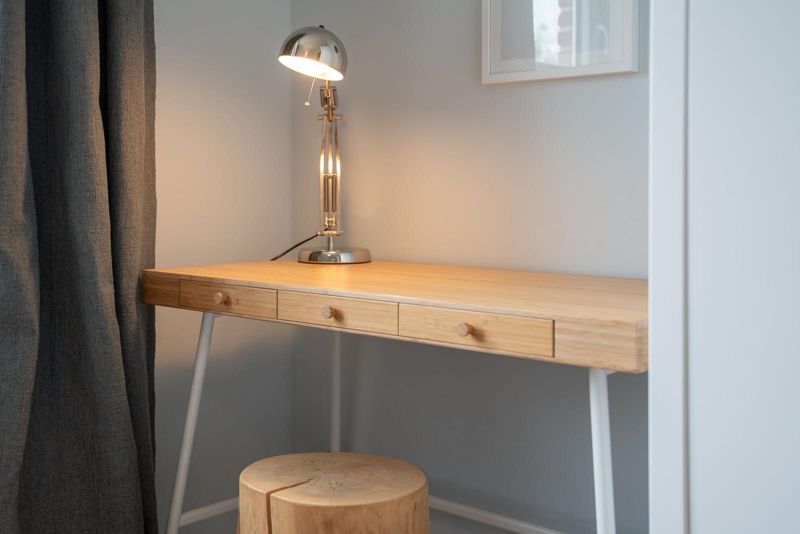 Schreibtisch mit drei Schubladen und Stuhl. Lampe und Bild an der Wand.