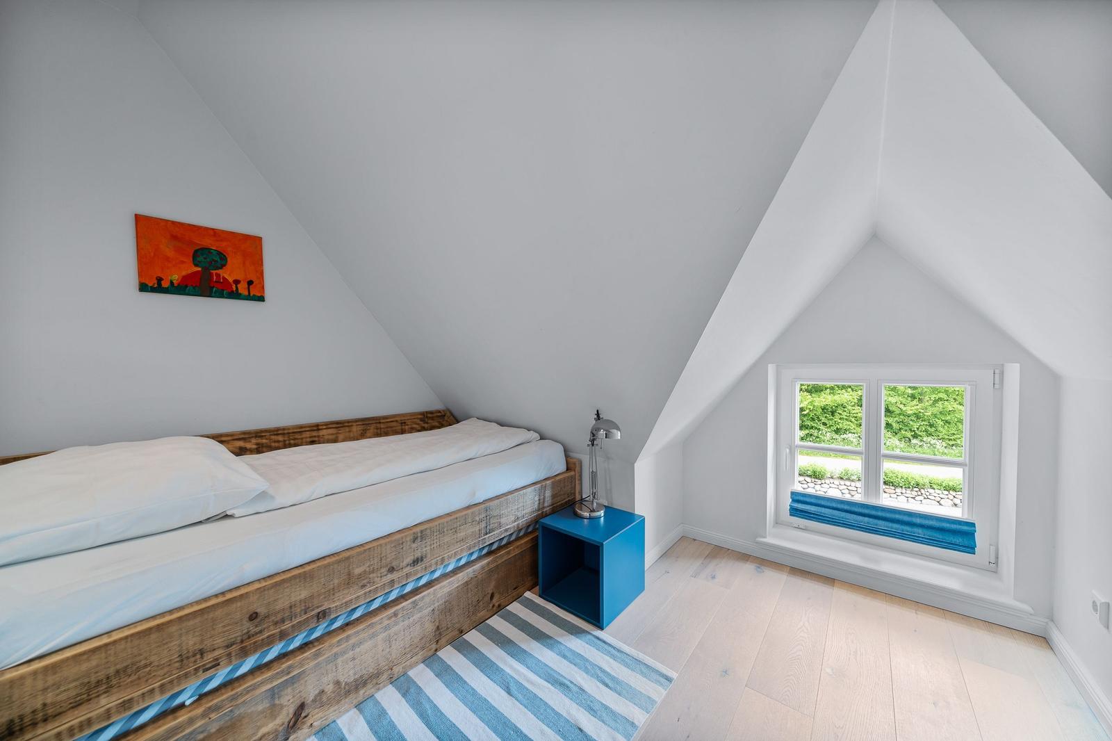 Ein Schlafzimmer mit Holzbett, blauem Nachttisch und Fenster mit Blick auf Grün.