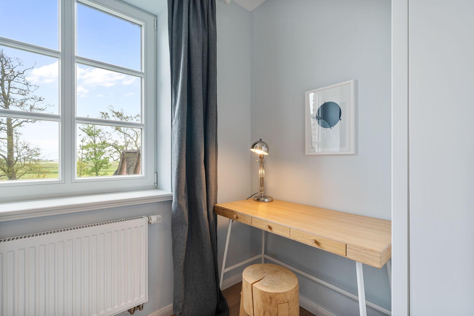 Schreibtisch mit Stuhl und Lampe neben Fenster mit Blick auf Landschaft.