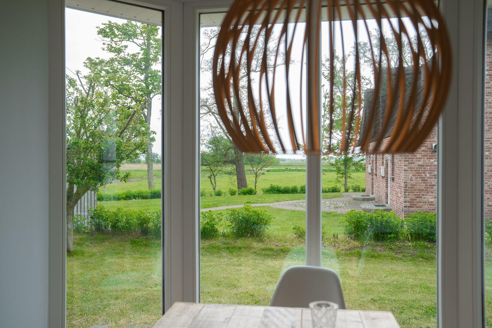 Durch große Fenster blickt man auf einen grünen Garten mit Bäumen und eine Backsteinmauer.
