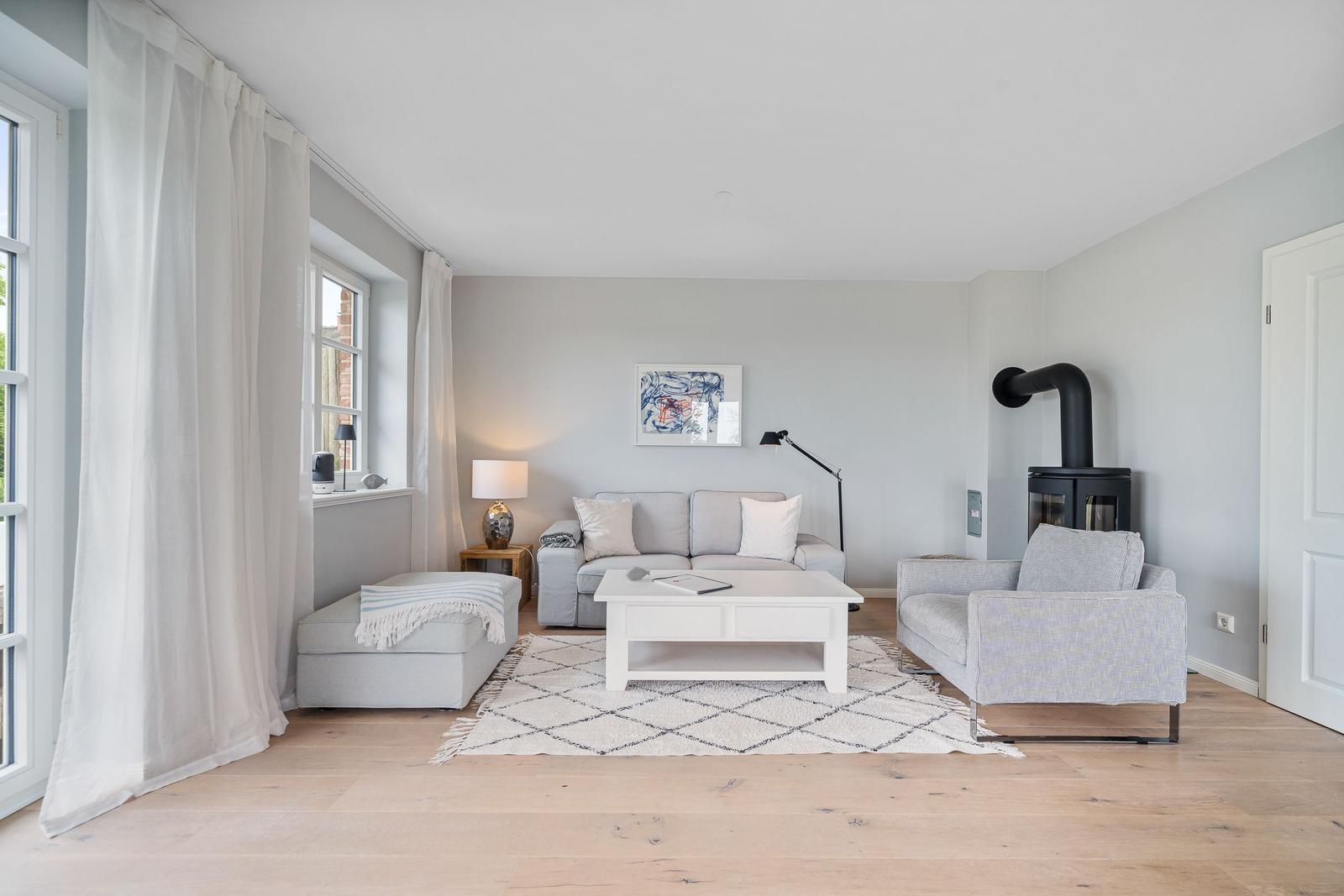 Wohnzimmer mit Sofa, Sessel und Kaminofen. Holzboden und helle Wände.