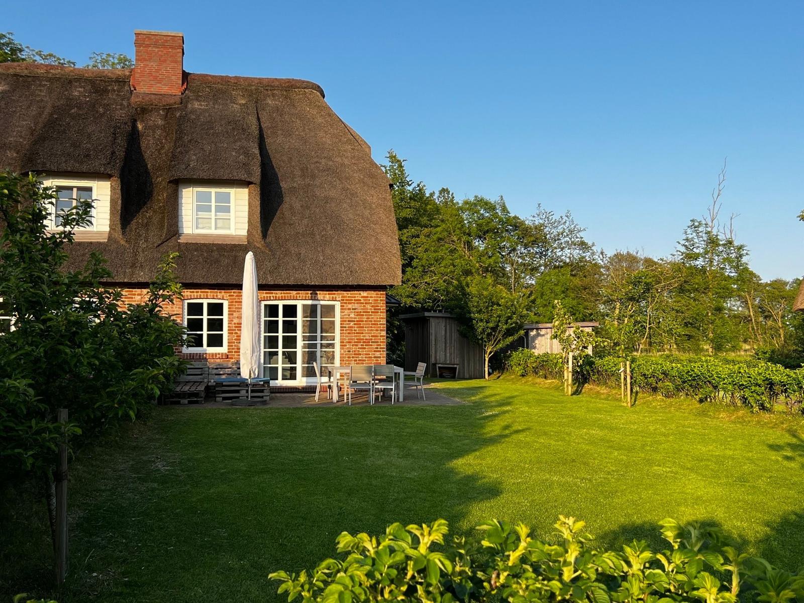 Haus mit Strohdach, Terrasse und Garten. Holzhaus mit weißen Fenstern und Türen.