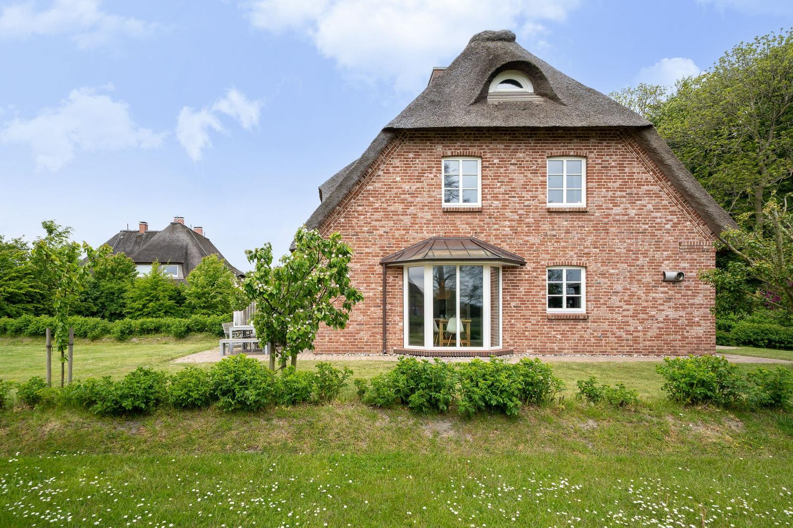 Rotes Backsteinhaus mit Strohdach und Fensterfront im Garten.