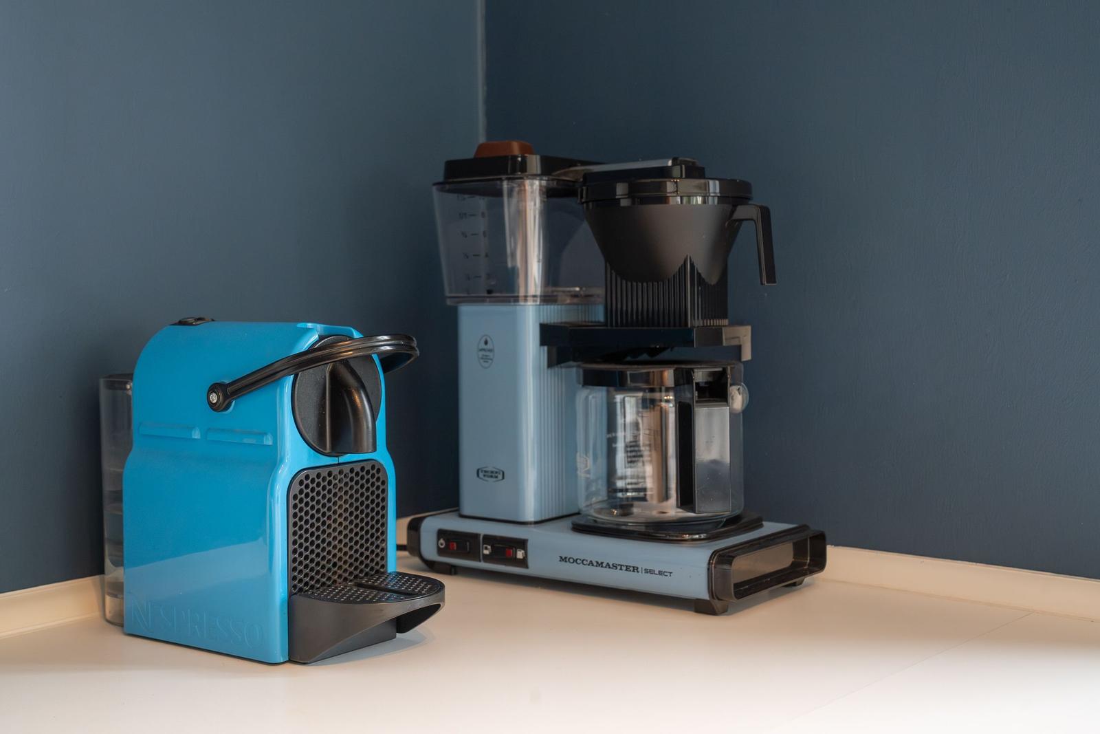 Eine blaue Nespresso-Kaffeemaschine und eine Moccamaster-Kaffeemaschine auf einer Arbeitsplatte.