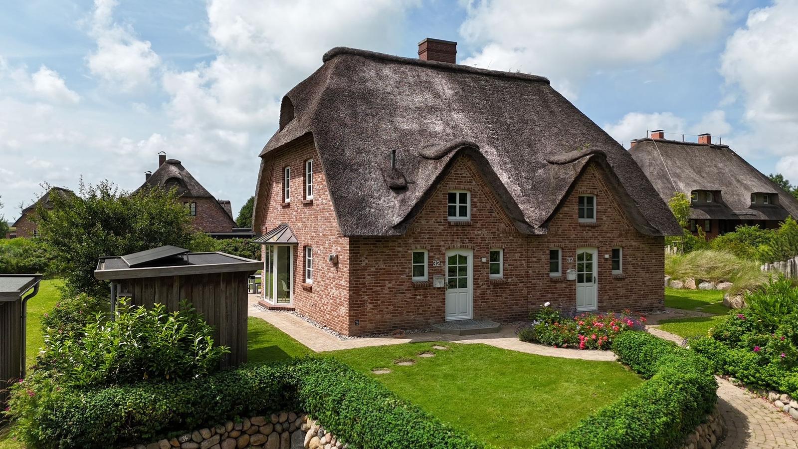 Ein Haus mit strohgedecktem Dach, roten Ziegeln und einem gepflegten Garten.
