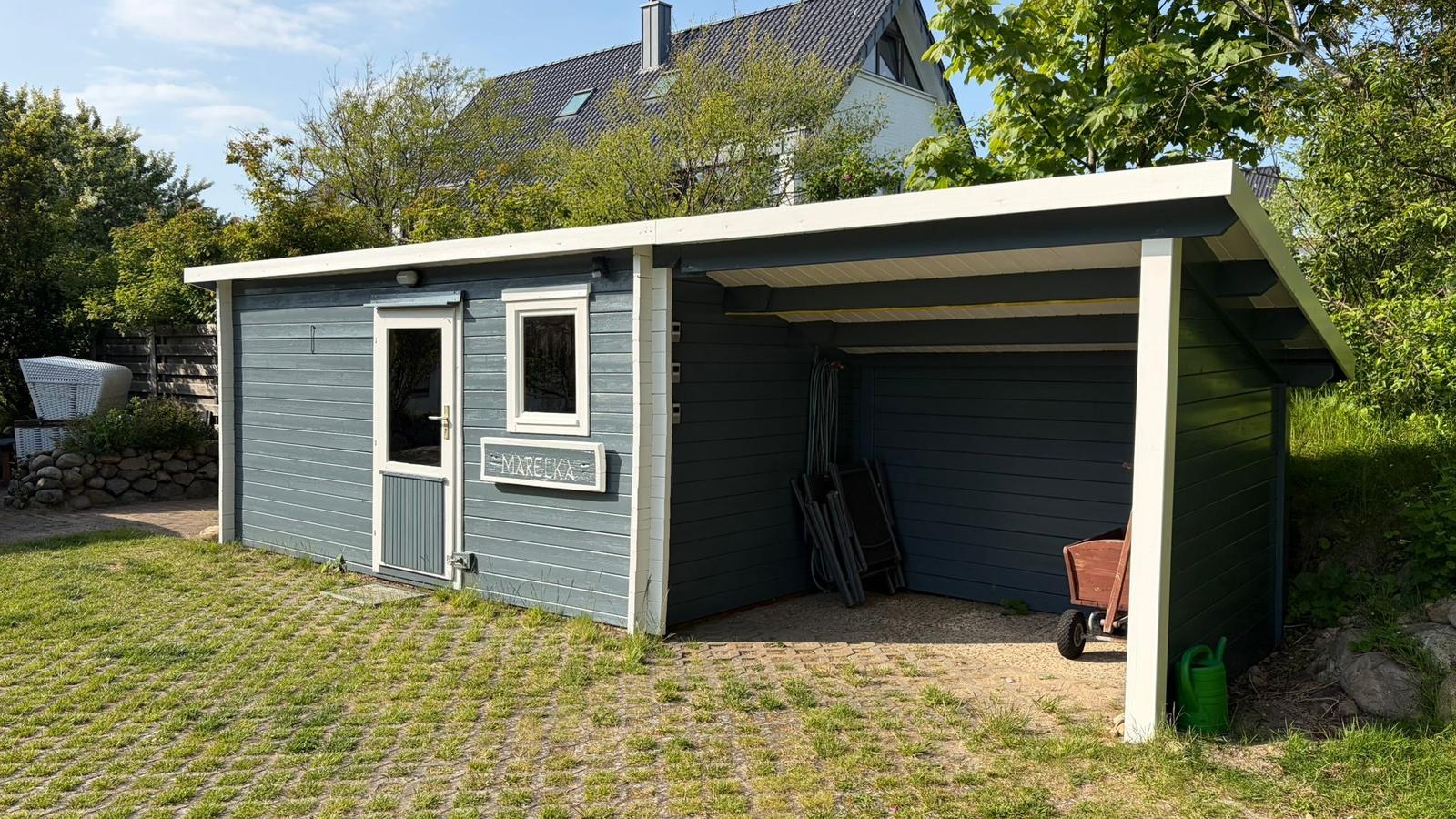 Gartenhaus mit Überdachung und Eingangstür. Auf dem Grundstück steht ein Gartenhäuschen mit Schutzdach.